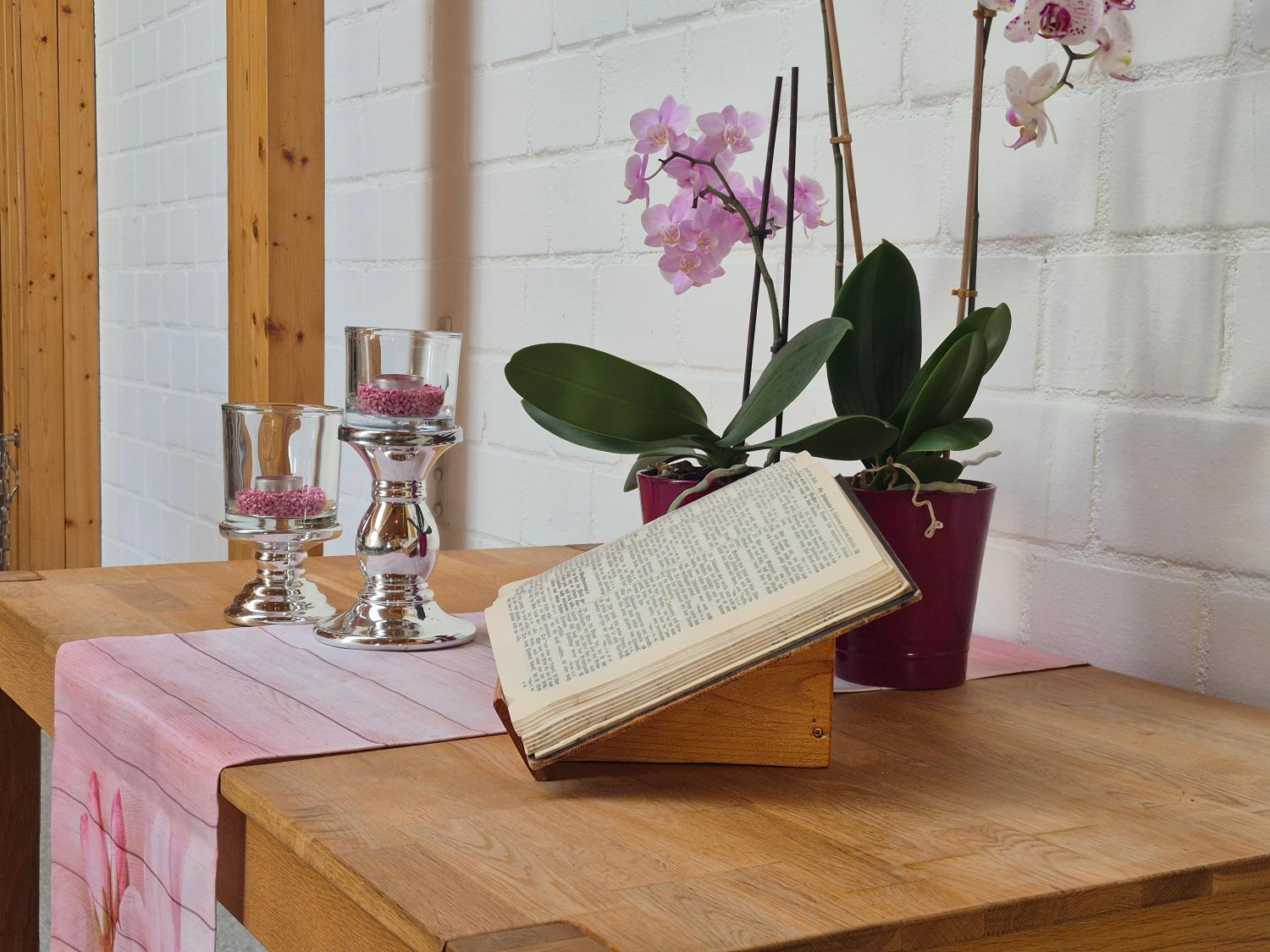 Seitenansicht auf ausgestellte offene Bibel mit zwei Kerzen und einer Topfpflanze im Hintergrund