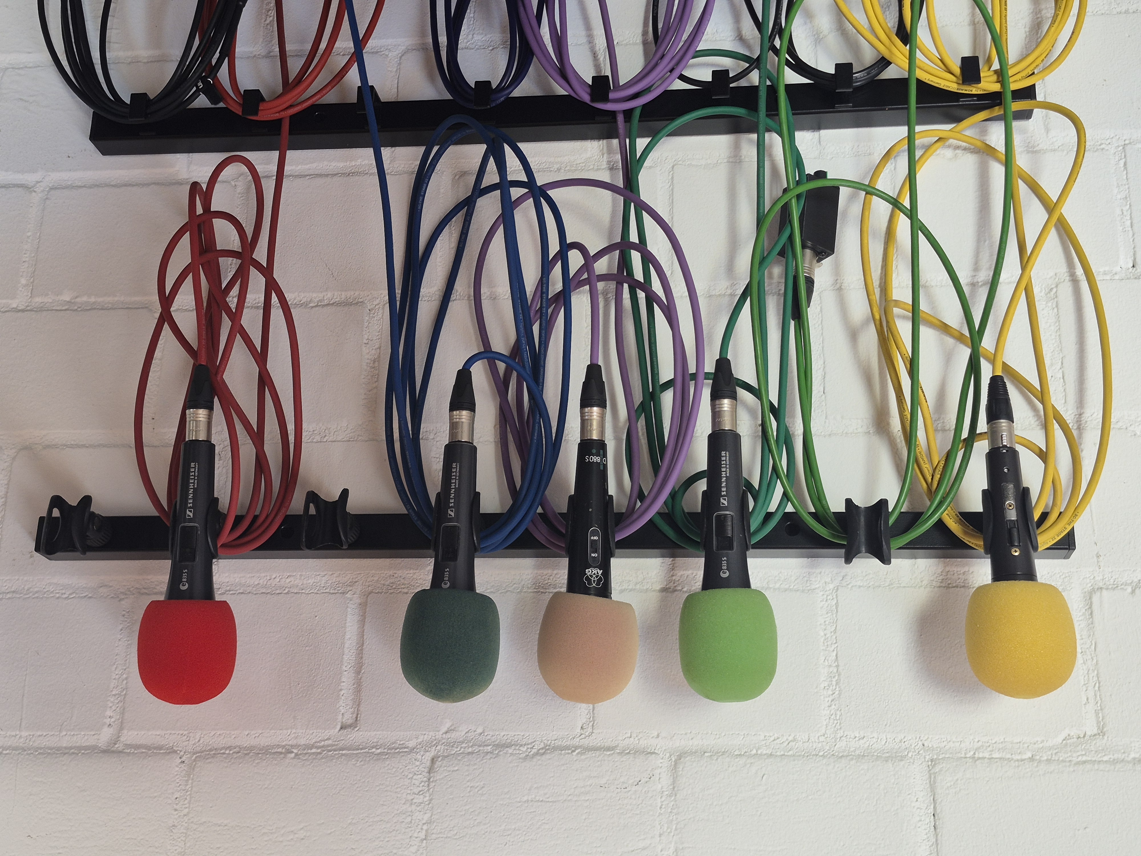 5 Mikrofone mit buten Kabeln an einer Wandhalterung aufgeräumt aufgehangen